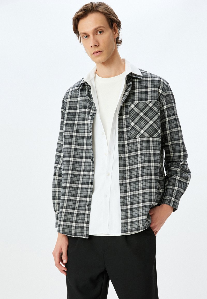 Rutig button-up skjorte i sort, hvid og grå med en brystlomme og krave over en hvid crew-neck skjorte. Blandingsstof af bomuld.