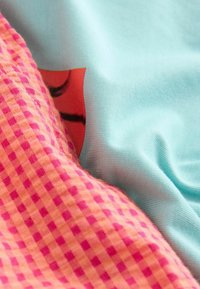 Tissus pliés montrant un tissu à carreaux rose et orange à côté d'un tissu bleu clair avec un petit détail imprimé rouge et noir.