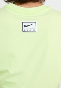 Svetlo zelena bombažna majica s kratkimi rokavi in okroglo ovratnikom, ki ima na zadnji strani v središču pravokotni črno-beli etiket Nike "TEAM".