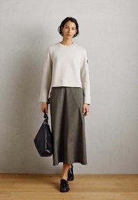 Sudadera recortada gris claro, falda midi verde oliva, mocasines negros y un bolso negro texturizado. Diseño simple, textura suave y colores neutros.