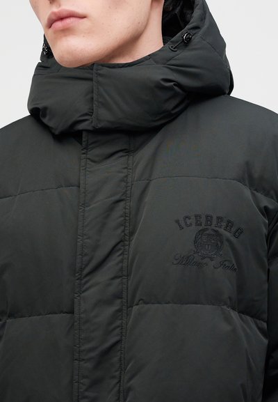 Homme portant une veste matelassée noire avec un col montant et une capuche, avec un logo brodé "ICEBERG Milano Italia" sur la poitrine.