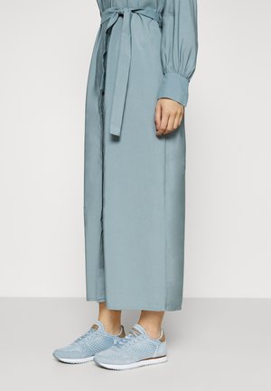 Persona que lleva un vestido largo azul claro con un cinturón atado y zapatillas deportivas a juego azul claro con suelas blancas.