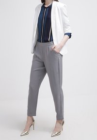 Bílý blazer přes námořnickou a krémovou pruhovanou blůzu, spárovaný se šedými kalhotami a zlatými podpatky. Hladká tkanina, přiléhavý střih a elegantní design.