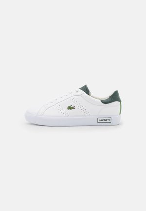 Zapatilla blanca de corte bajo con lengüeta verde en el talón, laterales perforados, logo del cocodrilo de Lacoste en el lateral y texto "Lacoste" en la suela blanca.