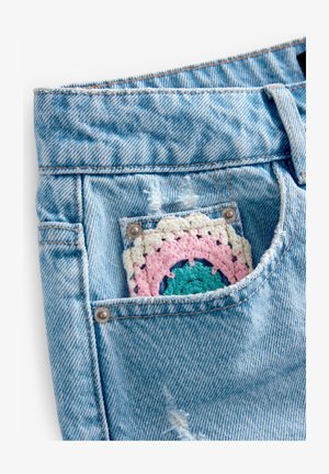 Svijetloplave traper šorts hlače s rasparanim rubovima i čipkastim zakrpama u ružičastoj, tirkiznoj i krem boji u stražnjem džepu. Vidljivi metalni zakovice.