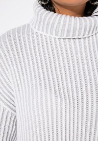 Weißer gerippter Rollkragenpullover mit vertikaler Strickstruktur, ausgestattet mit einem dicken umschlagbaren Kragen und weichem, dehnbarem Stoff.