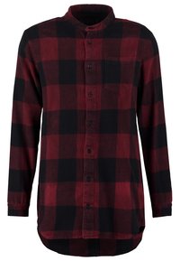 Chemise en flanelle à manches longues à carreaux rouges et noirs avec col mao, boutons sur le devant, poche poitrine et ourlet arrondi.