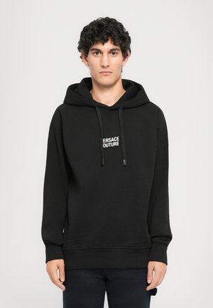 Sudadera con capucha negra con un parche de logo que dice "VERSACE COUTURE". Presenta puños y dobladillo de canalé, fabricada en un tejido suave y grueso.