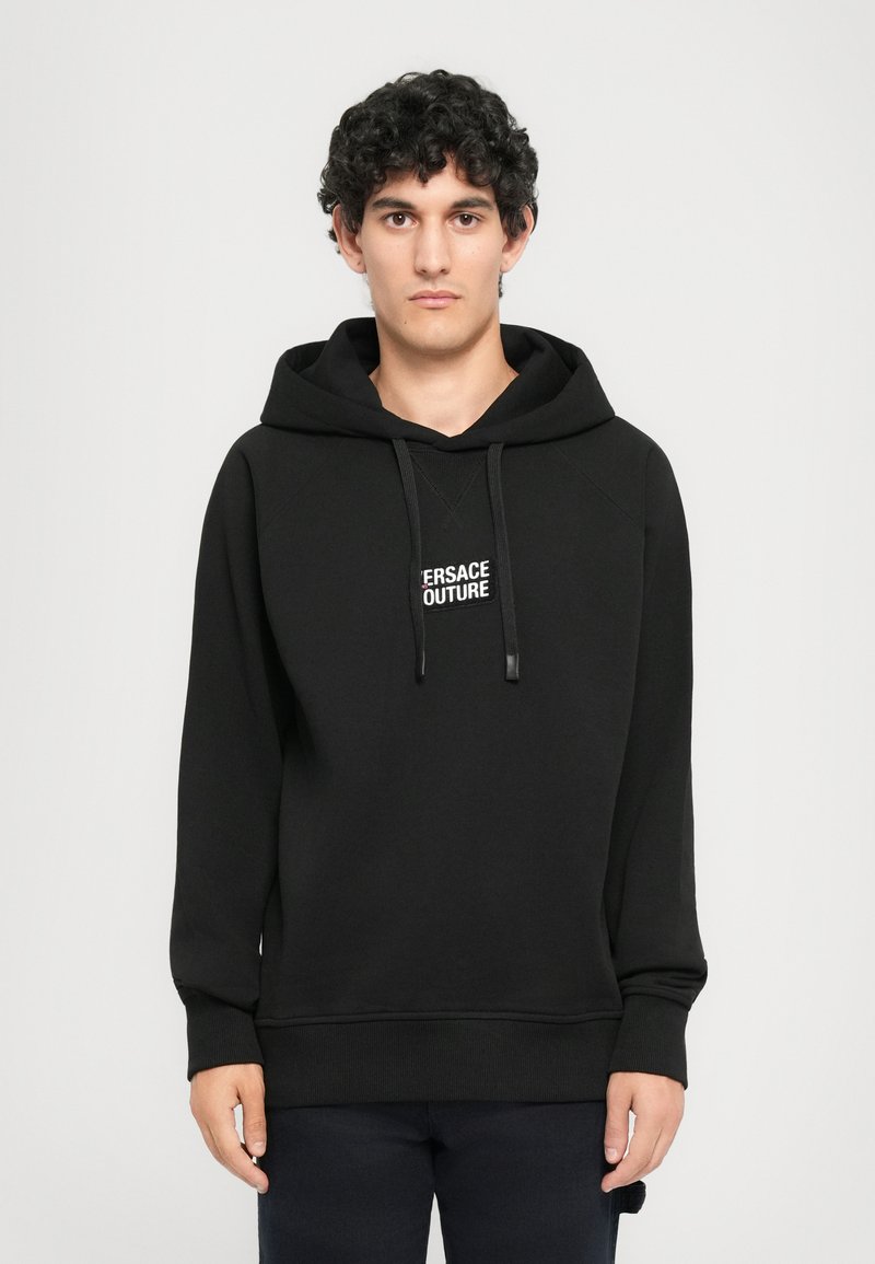 Čierna mikina s kapucňou a logom "VERSACE COUTURE." Obsahuje rebrované manžety a lem, vyrobená z jemnej, hrubej tkaniny.