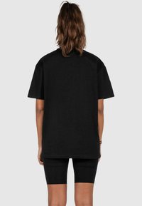 Sort oversized t-shirt vist fra bagsiden, med korte ærmer og en blød, glat tekstur. Kombineret med sorte cykelshorts.