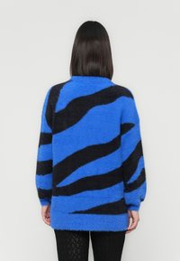 Suéter fofinho e oversized com listras onduladas em azul e preto. Apresenta mangas largas e uma bainha arredondada. Textura suave.