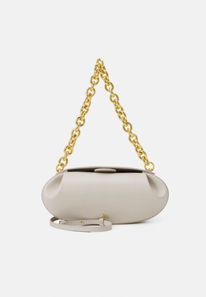 Oval geformte beige Handtasche mit einem großen goldenen Kettenriemen und einem abnehmbaren dünnen beigen Lederriemen vor einem einfachen Hintergrund.