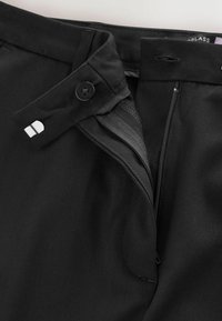 Black trousers featuring a front button closure, zipper fly, and fabric belt loop. Smooth texture with subtle stitching details.