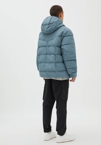 Puffjacka i ljusblått med huva, quiltat mönster och elastiska ärmslut, tillsammans med svarta cargobyxor och vita sneakers.