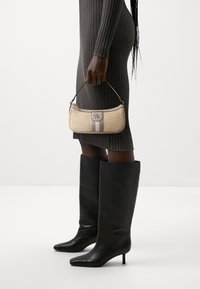 Bolso de mano tejido beige con una franja gris, un detalle de logotipo de metal y un asa corta, combinado con botas de cuero negro hasta la rodilla.