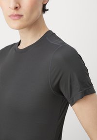 Camisa deportiva negra texturizada de manga corta, con un escote redondo y un sutil logo de la marca en la manga.