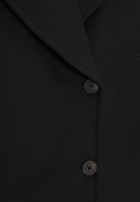 Sort blazer med tekstureret stof, notched revers og to knapper med fire huller. Inkluderer en påsyet lomme foran.