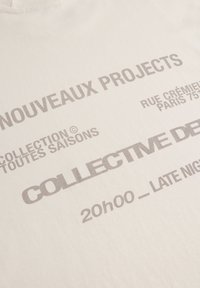 Off-white cotton t-shirt with gray printed text. Features details like "Nouveaux Projects," "Collective De," and event timing at the bottom.