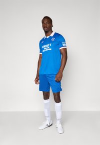 Blaues Fußballtrikot mit einem kurzärmligen Trikot mit weißen Akzenten und Sponsorenlogos, kombiniert mit passenden Shorts und weißen Socken mit einem Muster.