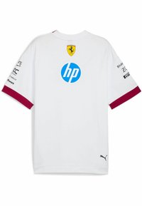 Cămașă albă cu mâneci scurte și accente vișinii; prezintă logo-ul Ferrari și brandingul HP. Fabricată dintr-un material cu o textură netedă; logo-ul Puma la margine.