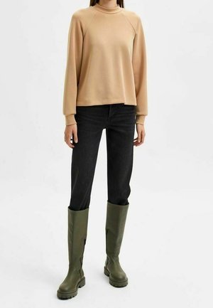 Beige sweatshirt met lange mouwen, gecombineerd met een zwarte spijkerbroek en groene leren laarzen tot de knie met een gestructureerde zool.