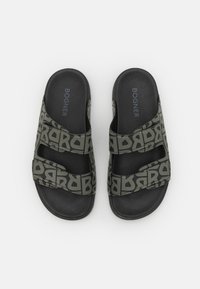 Sandales noires à glissière avec deux straps ajustables, présentant un motif logo gris répétitif. Semelle intérieure texturée pour le confort.
