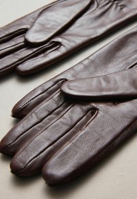 Braune Lederhandschuhe mit glatter Textur, passgenauem Design und detaillierter Naht entlang der Nähte. Dünner, fingerloser Stil.