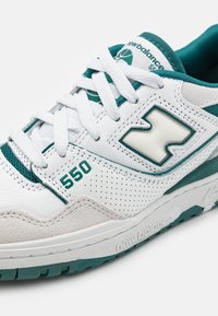 Baskets en cuir blanc avec des accents teal et des détails en maille. Présentent une boîte à orteils perforée, une semelle épaisse et "550" sur le côté.