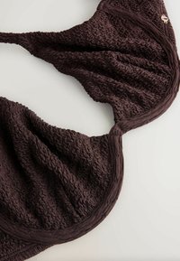 Top de bikini maro închis cu textura, cu material adunat (ruched) și bretele ajustabile, așezat plat pe o suprafață deschisă la culoare.