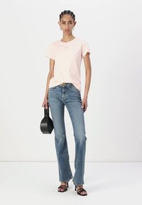 Rozā kokvilnas t-krekls ar īsām piedurknēm un mazu logotipu, apvienots ar zilām platām džinsām un melniem siksnu papēžiem. Modelis tur melnu somu.