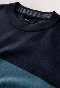 Sötétkék kötött pulóver világos türkiz vízszintes csíkkal. Bordázott nyakkivágással és "NEXT" feliratú címkével. Puha tapintású, minta nélkül.