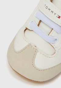 Hvit og beige sneakers med syntetisk overdel, med snøringsdesign, kontrastsøm og en logo på siden. Glatt tekstur.