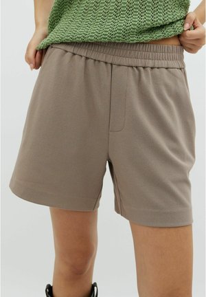 Gros plan d'une personne portant un short taupe à taille élastique et un haut en maille verte, les mains ajustant l'ourlet de la chemise.
