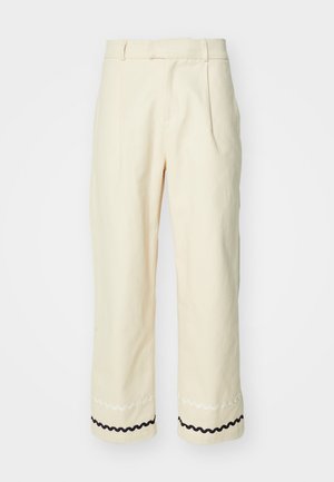 Kremowe spodnie o dopasowanym kroju, z plisami, w skróconym fasonie, z ozdobnym czarno-białym falistym wykończeniem na dole.