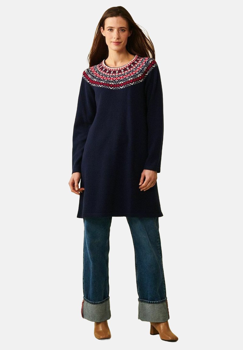 Marineblå uld sweaterkjole med et dekorativt rødt og hvidt mønster ved skulderen, med lange ærmer og en afslappet pasform, parret med flared jeans.