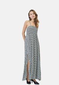 Rochie maxi cu un model alb-negru, cu bust smocked, bretele subțiri și fante laterale, asortată cu pantofi cu toc înalt negri.