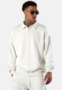 Cremefarbenes Sweatshirt aus weichem Stoff, mit einem Reißverschlusskragen, gerippten Bündchen und einem dezenten Logo auf der Brust.