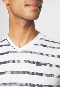 Vit V-ringad Nike t-shirt med horisontella svarta ränder, med en texturerad design och en liten svart logga på bröstet.