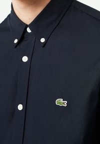 Polo shirt blu navy con colletto button-down e bottoni bianchi, con un piccolo logo di coccodrillo ricamato sul petto.