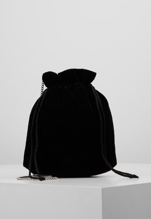 Czarna aksamitna torebka z ściągaczem, plecionymi sznurkami oraz srebrnym łańcuszkiem, umieszczona na białym piedestale na jednolitym tle.