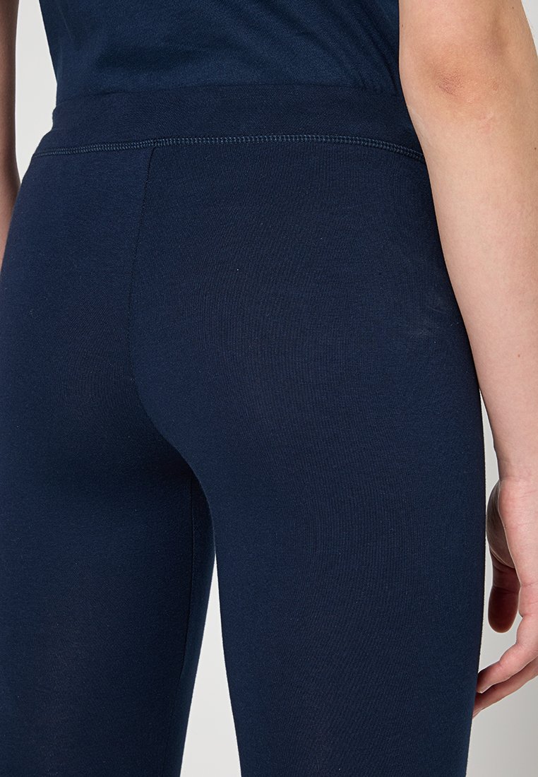 Primo piano di una persona che indossa leggings blu navy aderenti e una maglietta abbinata, mostrando la parte bassa della schiena e le cosce superiori.