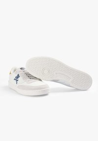 Witte leren sneakers met lichtgrijze suède accenten, een blauw logo en een gemêleerde witte rubberen zool met een geometrisch patroon.
