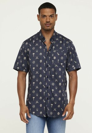 Chemise à manches courtes en coton bleu foncé avec des imprimés graphiques clairs incluant des crânes, des palmiers et des perroquets. Dispose d'une poche poitrine.