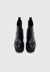 Musta nahkainen Chelsea-saapas, jossa on joustavat sivut, pyöreä kärki ja paksu pohja. Takana vetoremmit, jotka helpottavat pukemista.