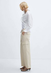 White shirt with a slim fit, long sleeves, and rolled cuffs. Beige cargo pants with side pockets and a relaxed wide-leg design. Black sandals.