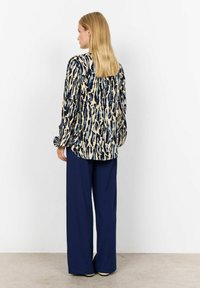 Blusa a maniche lunghe con motivo nei colori crema, blu e nero, abbinata a pantaloni navy a gamba larga, caratterizzati da una trama liscia e una vestibilità comoda.