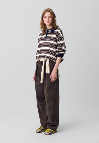 Maglione a righe in crema e marrone, con colletto blu navy; abbinato a pantaloni marrone a righe sottili. Presenta scarpe argento con lacci gialli.