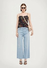 Μαύρα λουλουδάτα αμάνικα μπλουζάκια με λεπτές τιράντες, ανοιχτό μπλε παντελόνια με φαρδιά πόδια, μαύρες σανδάλες με λουράκια και μια μικρή μπεζ τσάντα ώμου.