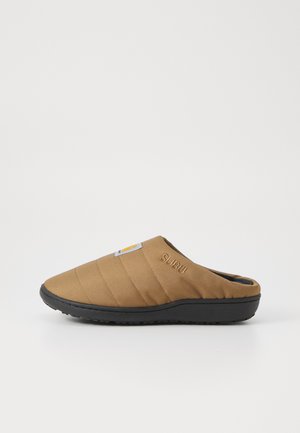 Brązowe materiałowe buty wsuwane z pikowanym wzorem, czarną gumową podeszwą i haftowanym logo "SURU" z boku.