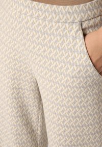 Lightly patterned trousers featuring a geometric design in beige and gray tones, with a soft texture and side pocket detail.